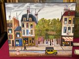 une photo d'un tableau représentant une scène de rue, posé sur une table
