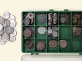 une boîte verte remplie de nombreuses pièces, à côté d'un tas de pièces