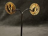 a pair of gold earrings on a stand against a black background