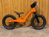 un vélo d'équilibre orange adossé à un mur en bois, devant un mur en bois