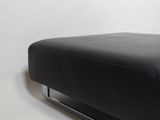 a black leather ottoman with chrome legs on a white background