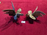 two figurines of birds on display on a red surface