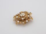 a close up of a gold and pearl broochle on a white surface