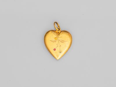 un pendentif en forme de cœur en or orné d'une petite pierre rouge