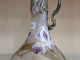 un vase en verre muni d'une poignée en argent, posé sur une étagère
