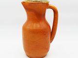 a small orange pitcher with a handle on a white surface