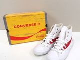 une paire de Converse rouges et blanches posée à côté d'un carton de Coca-Cola