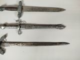 three silver colored swords on a white surface with a white background