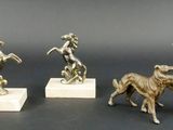 trois figurines en bronze représentant un chien et une femme, posées sur un socle