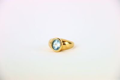 une bague en or sertie d'une topaze bleue repose sur une surface blanche