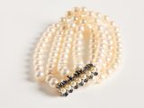 a close up of a bracelet with pearls and sapphires on a white surface