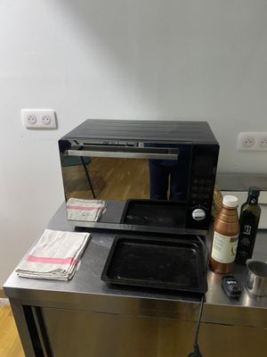 un micro-ondes posé sur un plan de travail en métal, à côté d'une bouteille de vin