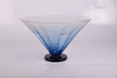 un bol en verre bleu avec un socle noir posé sur une surface blanche