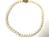 un gros plan sur un collier de perles blanches orné d'une fleur rouge