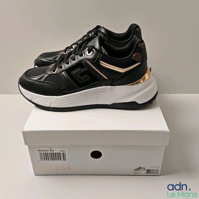 une paire de baskets noires et dorées posée sur une boîte blanche