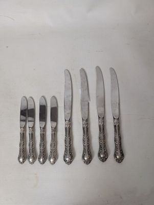 six silverplated knives and six knives are lined up on a white surface