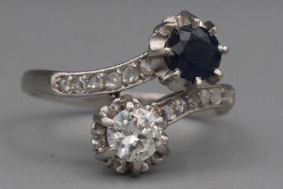 une photo d'une bague sertie d'un diamant et d'un saphir posée sur une surface grise