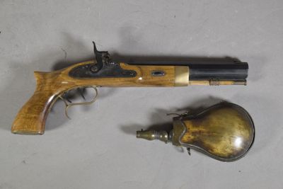 un vieux pistolet et une cloche en laiton posés sur une surface blanche