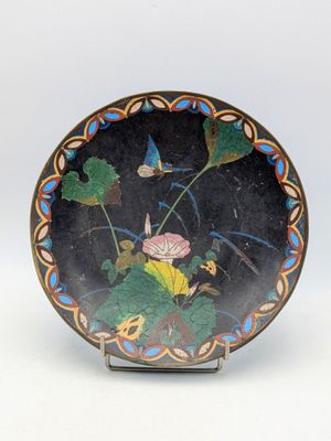 une assiette noire sur laquelle est représentée une fleur et des feuilles