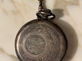 a silver pocket watch on a chain on a marble surface