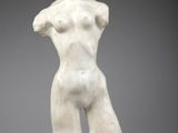 une sculpture blanche représentant un torse féminin posé sur un rocher