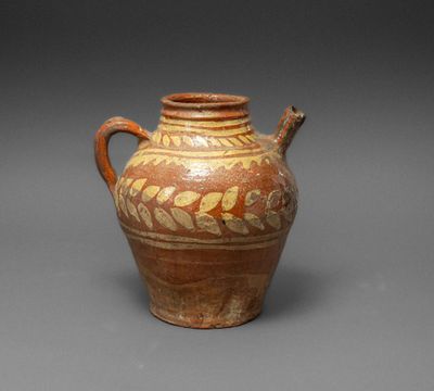 an old brown and white vase with a handle on a gray surface
