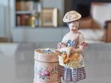 une figurine représentant une femme avec un panier de fleurs posé sur une table