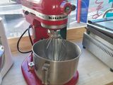 un robot de cuisine rouge posé sur un plan de travail, à côté d'une boîte de beignets