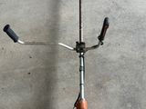 une trottinette posée par terre, avec une poignée fixée dessus