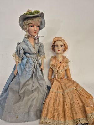 two dolls of women in dresses and hats are standing next to each other