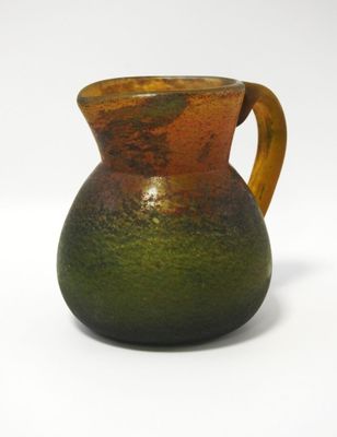 un vase marron et vert muni d'une anse, posé sur une surface blanche