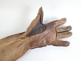 Quelqu'un tient une paire de gants en cuir marron posée sur une surface blanche.