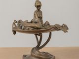 bronze statue of a boy sitting on a leaf with a dog on it
