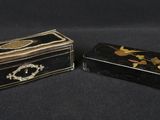 deux boîtes noires et dorées ornées de fleurs, posées sur un fond noir