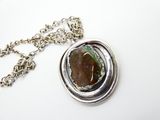 pendentif en argent orné d'une pierre verte, suspendu à une chaîne, sur un fond blanc