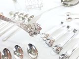une personne tenant une cuillère sur laquelle sont posées plusieurs cuillères en argent