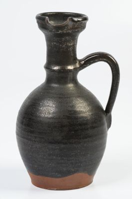 un vase noir muni d'une anse marron, posé sur une surface blanche