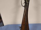 un fusil posé sur une nappe bleue, avec un mur blanc en arrière-plan