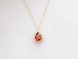 a gold necklace with a red tear shaped stone on a white background