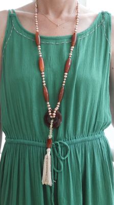 femme portant une robe verte et un collier orné d'une perle en bois et d'un pompon
