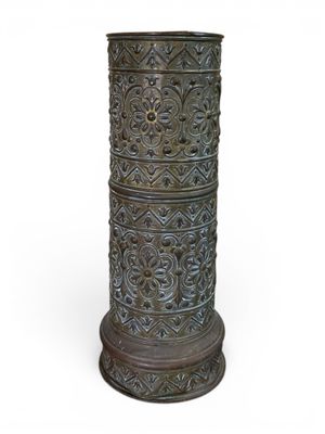une image représentant un grand vase en métal posé sur une surface blanche