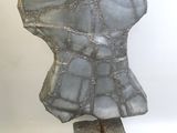 sculpture en pierre grise représentant un torse féminin, posée sur un socle