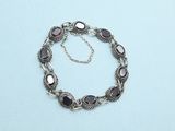silver bracelet with purple stones and a chain on a blue surface