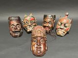 six carved wooden masks are arranged in a row on a table