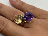 a person ' s hand holding a ring with two different colored stones