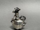 a silver figurine of a woman sitting on top of an apple