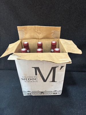 trois bouteilles de vin rouge dans une boîte en carton sur fond noir