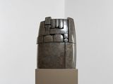 une sculpture dans un coin d'une pièce, avec une boîte posée par terre