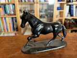 une statue représentant un cheval au galop posée sur une table en bois