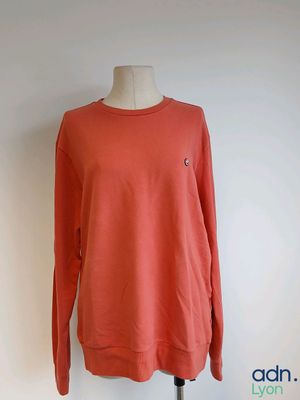 un pull orange posé sur un mannequin, devant un mur blanc